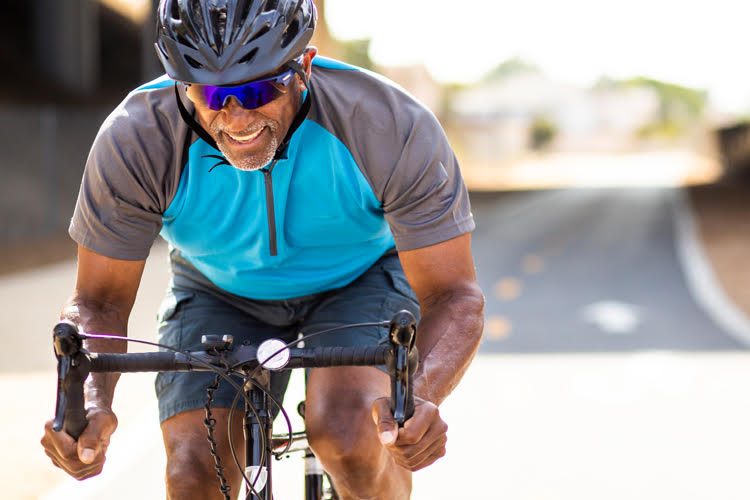 A physically fit guy in blue and grey shirt cycling on the road